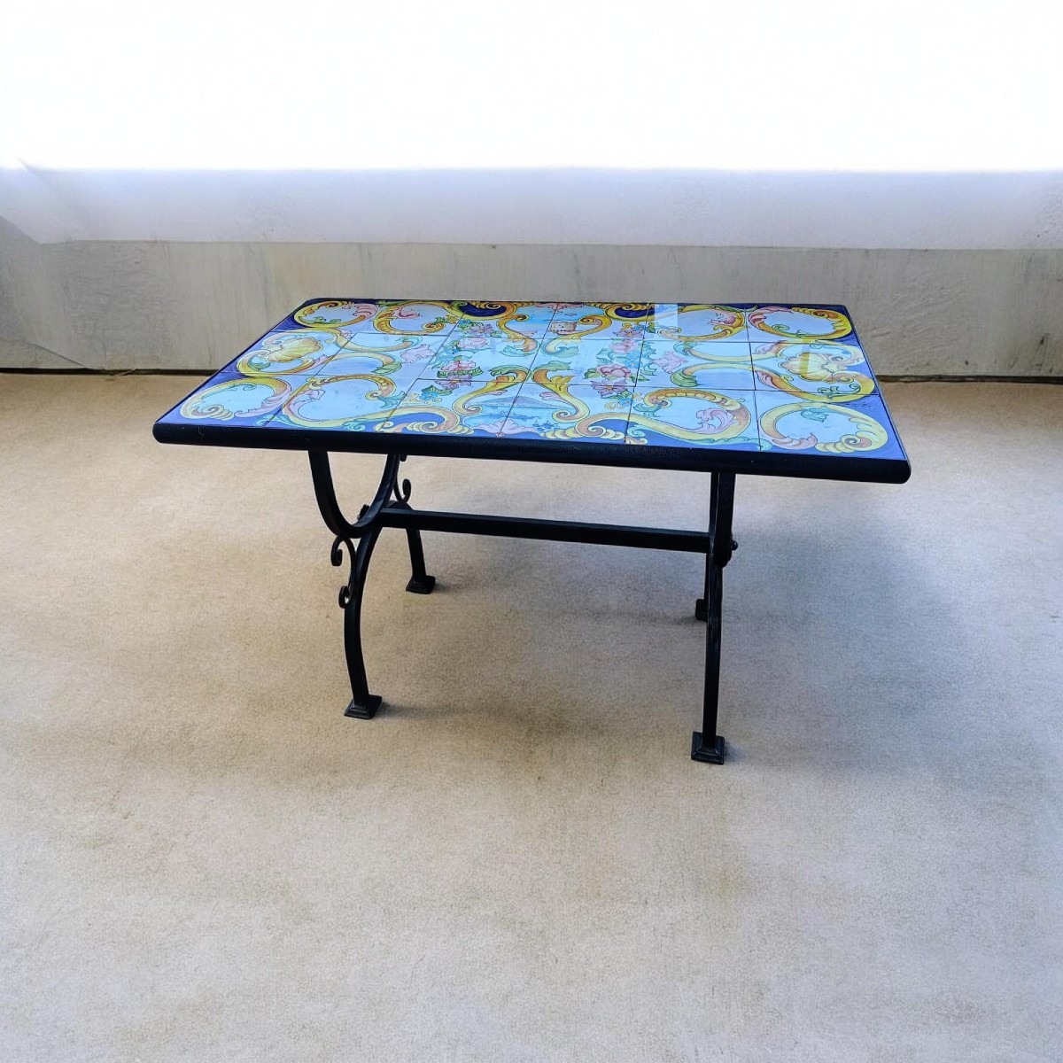 Tavolino artigianale con piano in ceramica maiolicata dipinta a mano e base in ferro battuto.