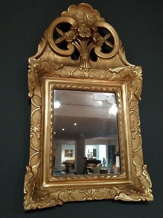 Specchiera in legno dorato ed intagliato. Motivi floreali ornano la ricca cimasa