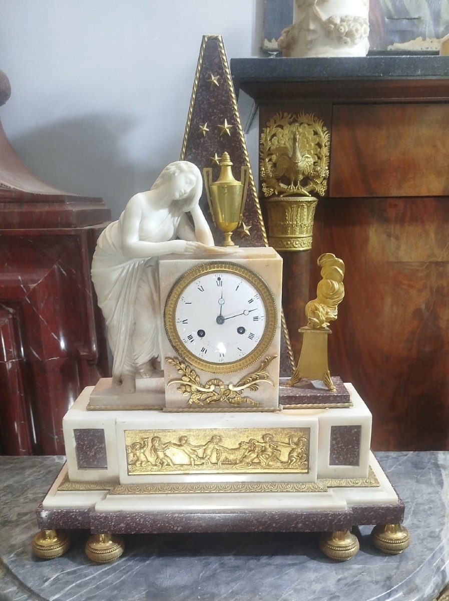 Orologio in marmo e porfido decorato con una vestale in marmo. inizio del XIX secolo
