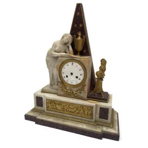 Orologio in marmo e porfido decorato con una vestale in marmo. inizio del XIX secolo