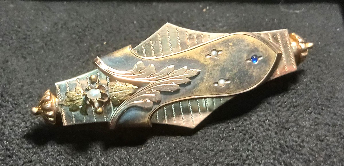 Spilla borbomica in oro 14 kt. con festone fogliaceo su fondo rigato.  