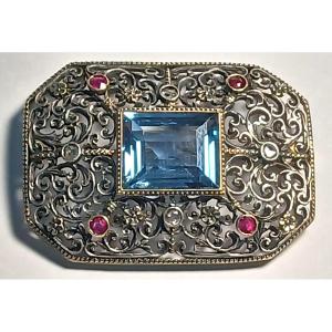  Spilla traforata a 'merletto' in oro e coppella, con topazio azzurro diamanti e rubini. Libert