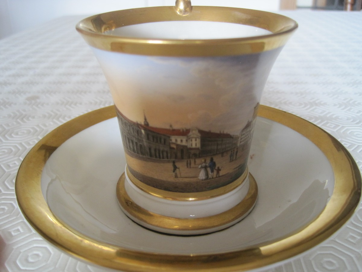 Tazza e piattino in porcellana dipinta con veduta di una piazza, Francia o Germania 1830 circa.