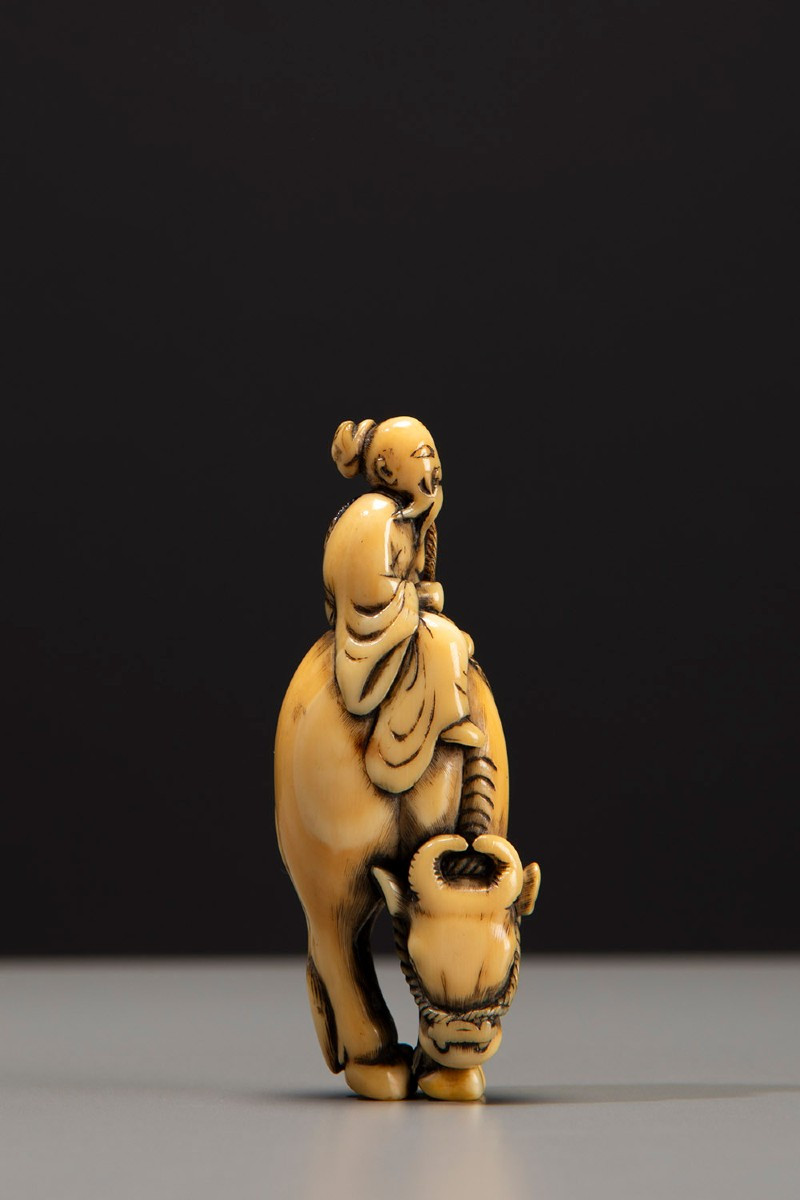Netsuke in avorio raffigurante Roshi seduto sul dorso di un bufalo