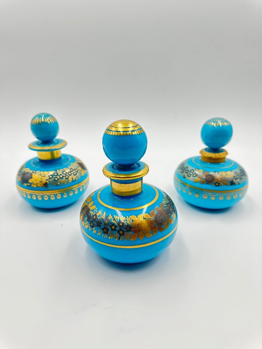 Set di tre bottiglie opaline blu turchese con decorazione dipinta di fiori dorati.